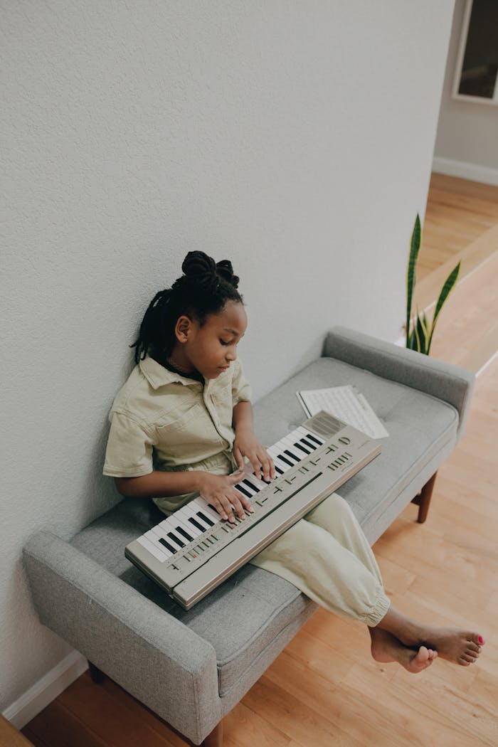 Child playing a keyboard indoors, seated on a bench in a peaceful home setting.